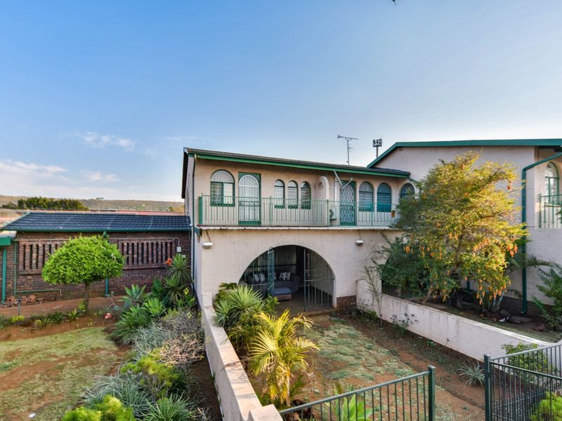 Rear view of the townhouse featuring a private garden, a covered patio area with an arched entrance, and an upper-level balcony with metal railings.