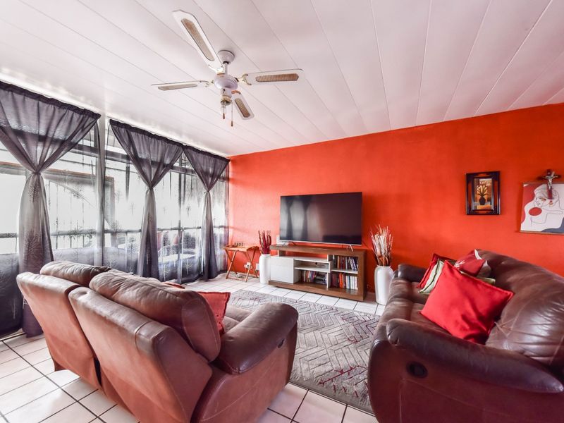 A living room featuring tiled flooring, a ceiling fan, and large windows that provide natural light.