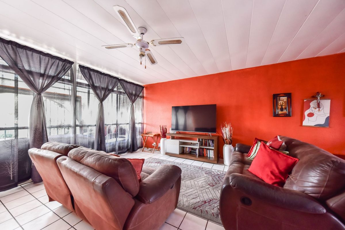 A living room featuring tiled flooring, a ceiling fan, and large windows that provide natural light.