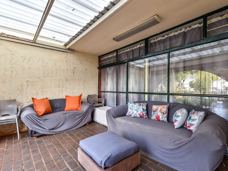 A covered patio area featuring brick flooring, a translucent roof, and large glass windows, providing a functional outdoor living space.