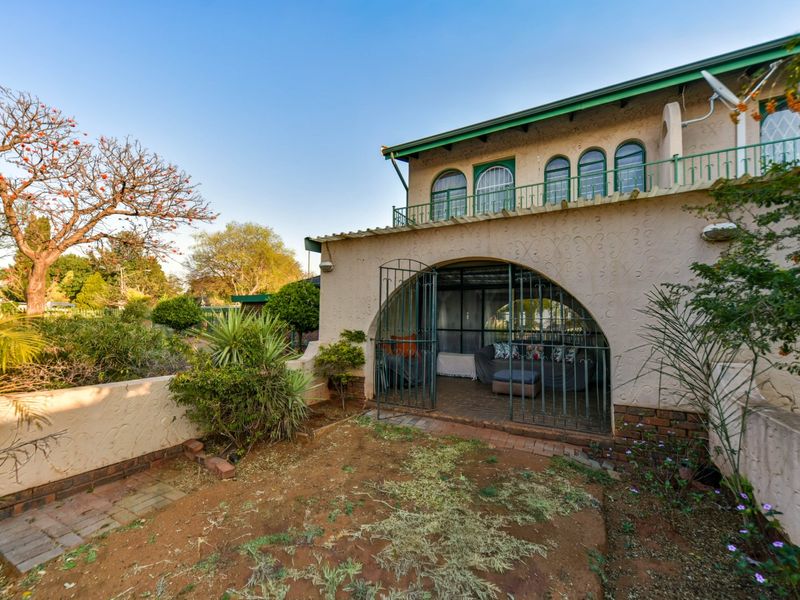 Rear view of the townhouse featuring a ground-level arched patio with security gate and an upper-level balcony with green metal railings.