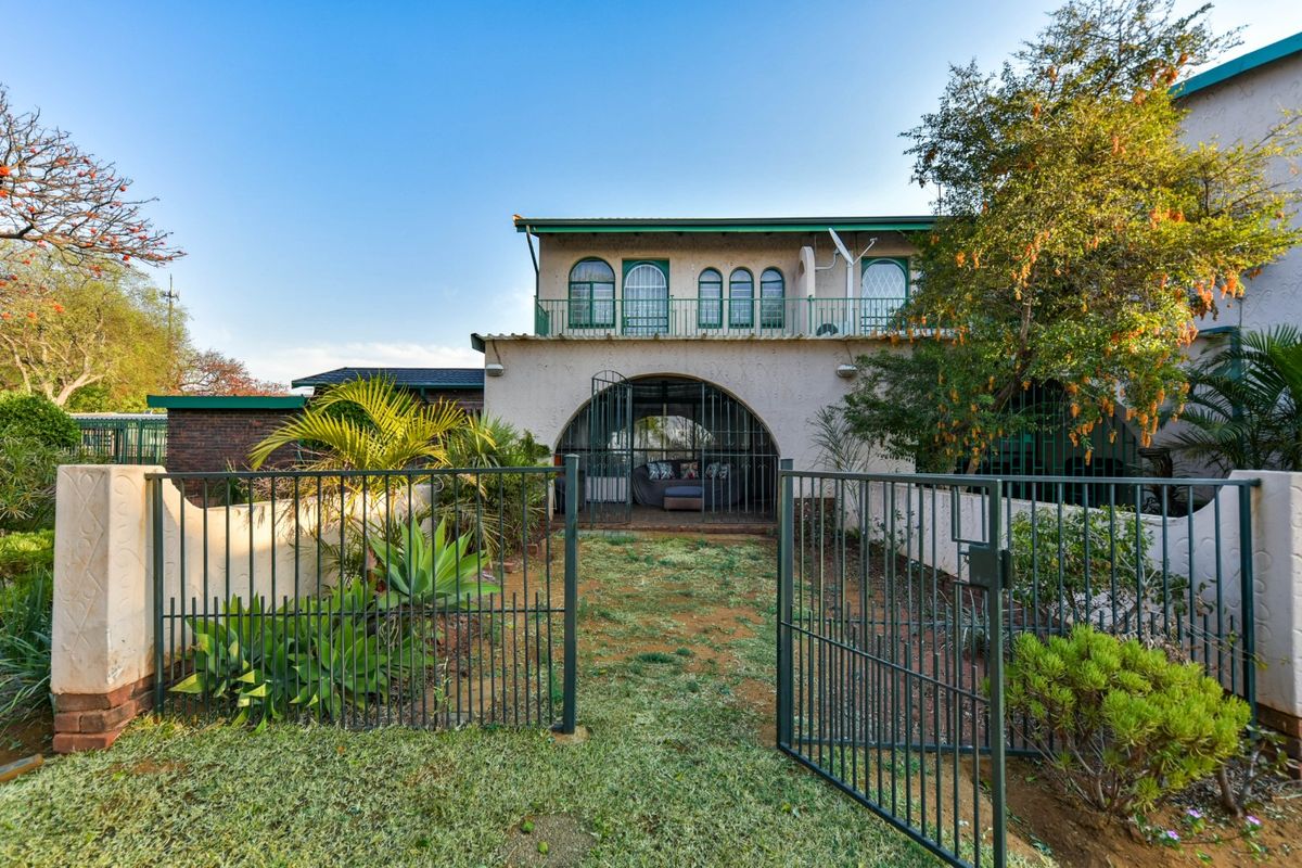 Rear view of the townhouse featuring a private garden, metal security gate, arched patio area, and an upper-level balcony with arched windows.