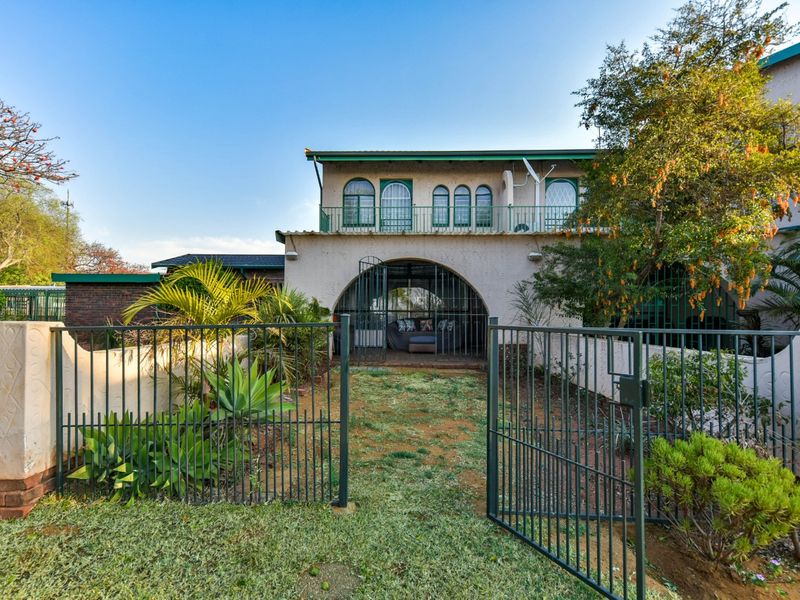 Rear view of the townhouse featuring a private garden, metal security gate, arched patio area, and an upper-level balcony with arched windows.