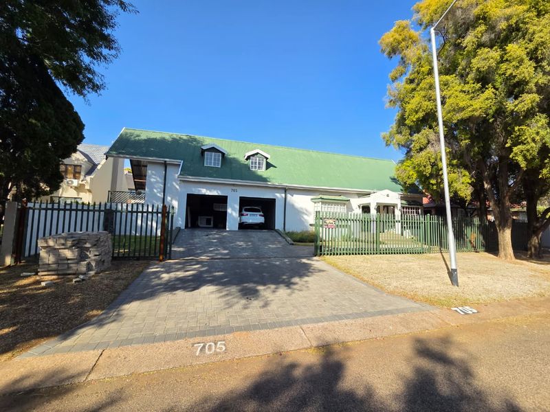 Front elevation of a house featuring a green metal roof, double garage, paved driveway, and secure metal perimeter fencing.