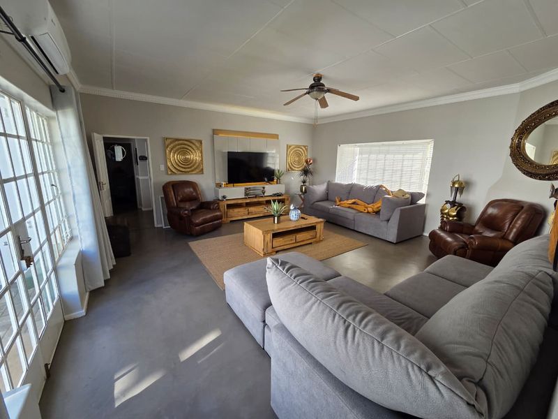 Spacious living room featuring polished concrete floors, a ceiling fan, split-system air conditioning, and large glass doors providing natural light.