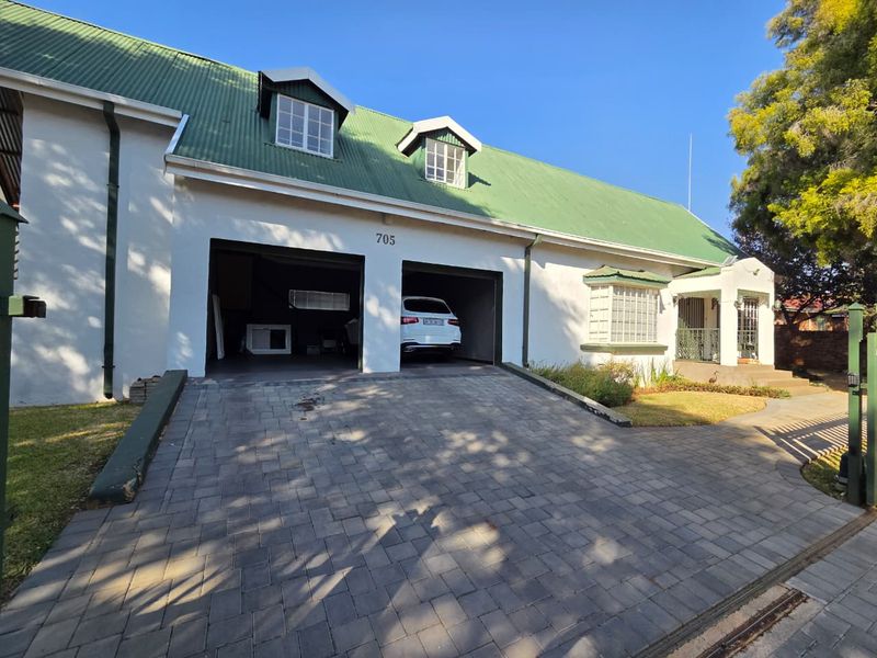 Front elevation of a house featuring a double garage, paved driveway, and a green metal roof with dormer windows.