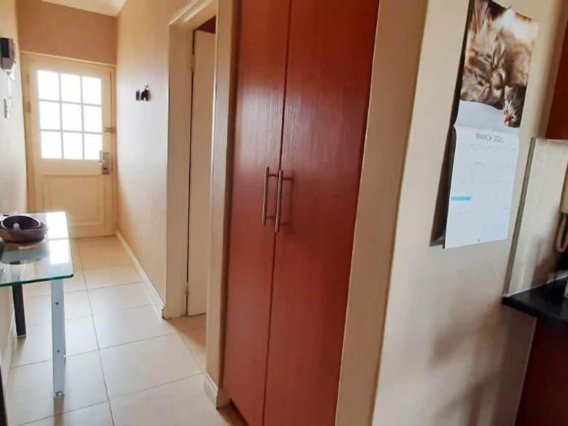 A functional hallway featuring tiled flooring and a built-in storage cupboard, providing access to the main entrance and adjacent living areas.