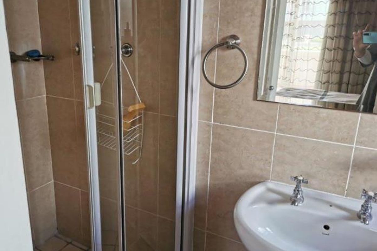 A functional bathroom featuring a shower enclosure, pedestal basin, and neutral wall tiling.