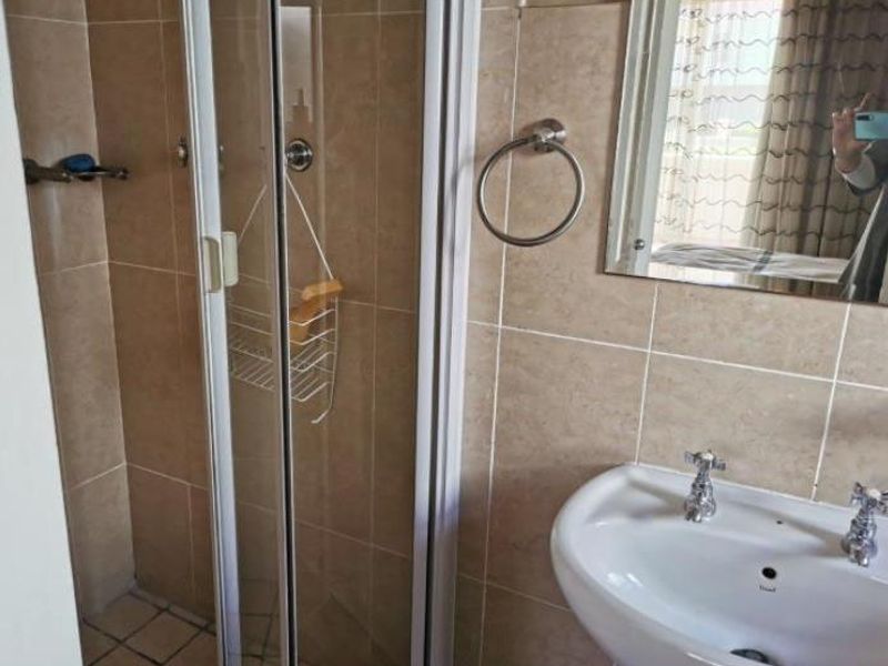 A functional bathroom featuring a shower enclosure, pedestal basin, and neutral wall tiling.