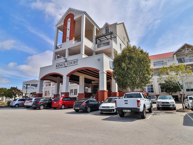 Front elevation of King's Court apartment complex featuring a prominent covered entrance, brick architectural accents, and an adjacent paved parking area.