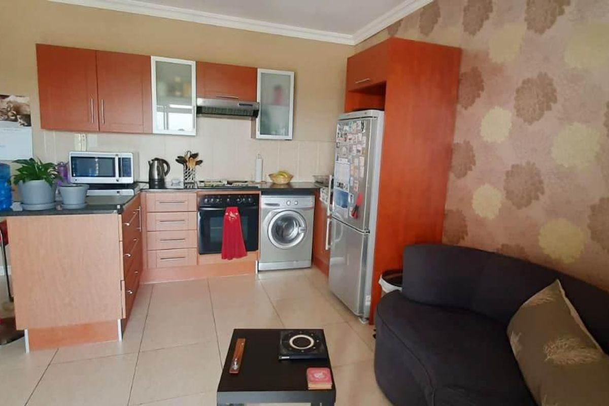 Open-plan kitchen and living area featuring wood-finish cabinetry, built-in oven, hob, extractor fan, and tiled flooring.