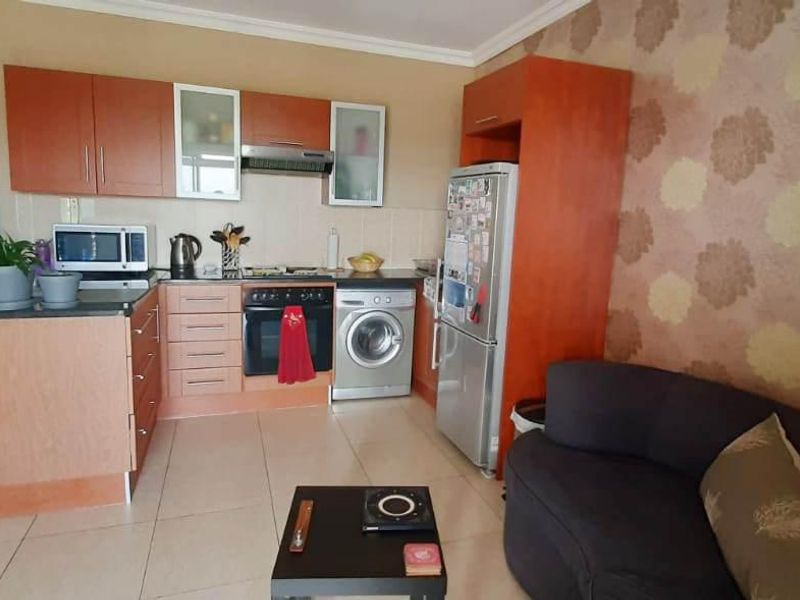 Open-plan kitchen and living area featuring wood-finish cabinetry, built-in oven, hob, extractor fan, and tiled flooring.