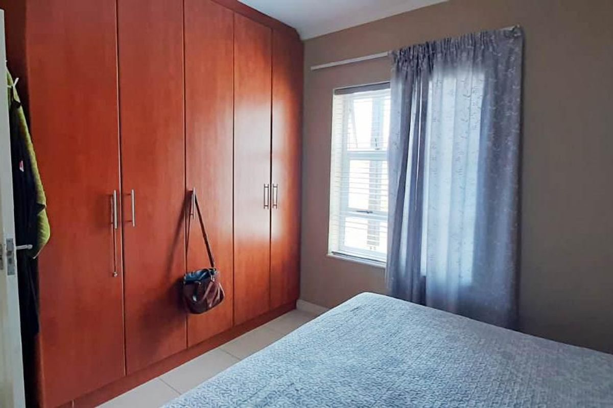 A bedroom featuring a large wooden built-in wardrobe, a window with curtains, and access to an adjacent room.