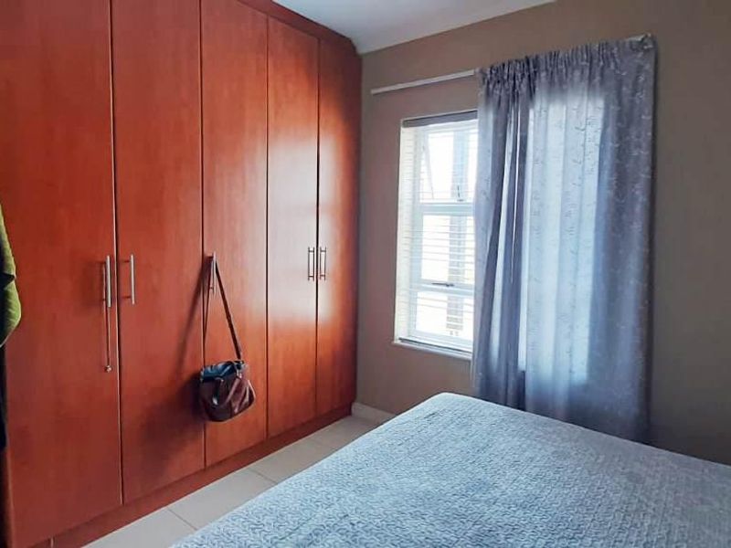 A bedroom featuring a large wooden built-in wardrobe, a window with curtains, and access to an adjacent room.