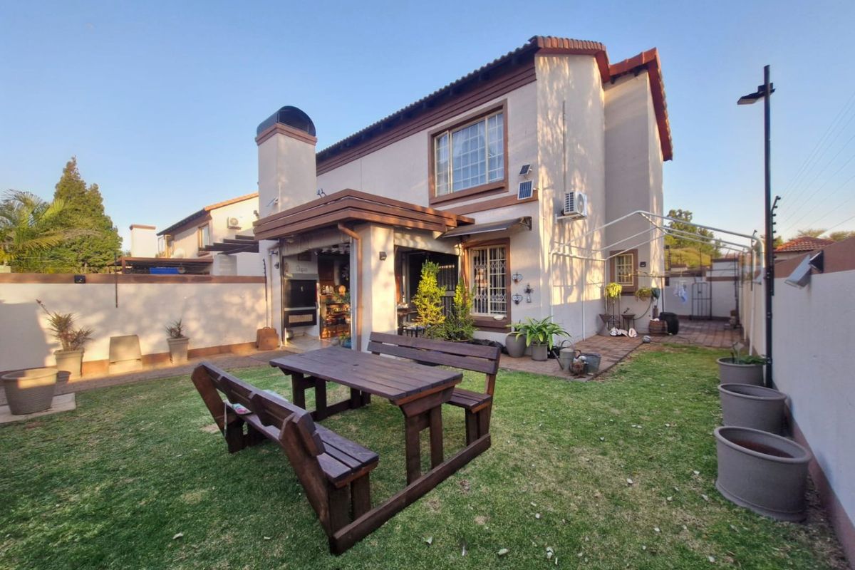 Rear view of the townhouse featuring a private garden, paved patio area with a built-in braai, and secure perimeter walling with electric fencing.