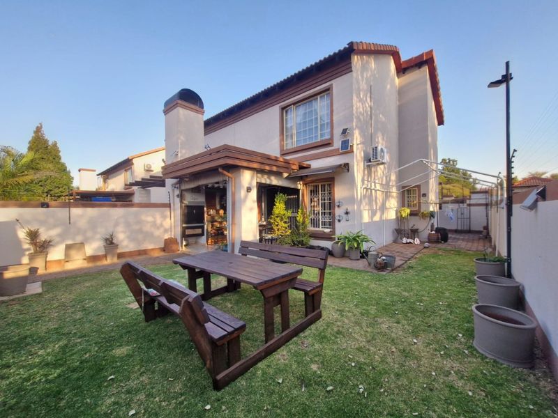 Rear view of the townhouse featuring a private garden, paved patio area with a built-in braai, and secure perimeter walling with electric fencing.
