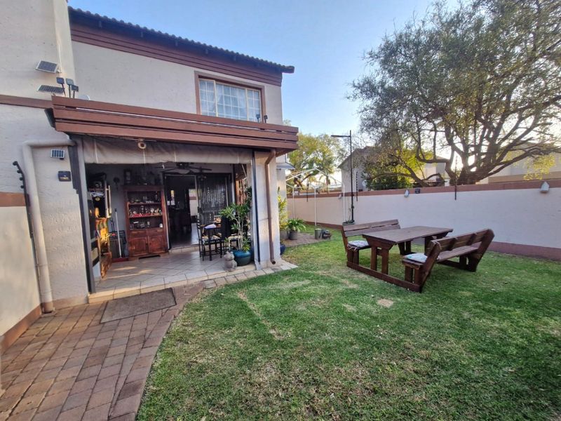 Rear view of the townhouse featuring a covered patio, paved walkway, and a private garden area enclosed by a perimeter wall with electric fencing.