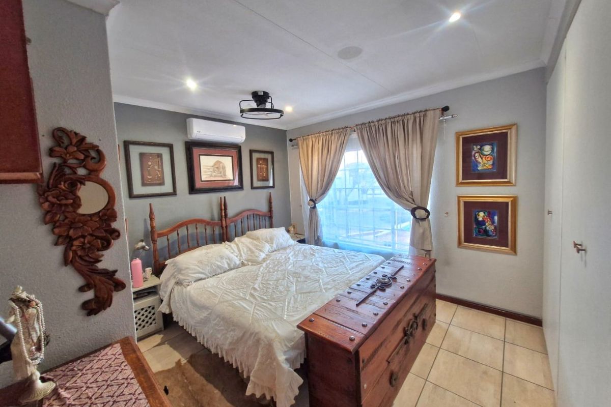 A well-maintained bedroom featuring tiled flooring, recessed downlighting, and a wall-mounted split-system air conditioning unit.