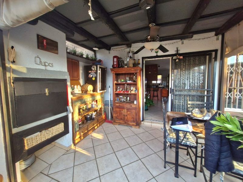 Covered patio area featuring a built-in braai, tiled flooring, and exposed beam ceiling, providing a functional outdoor entertainment space.