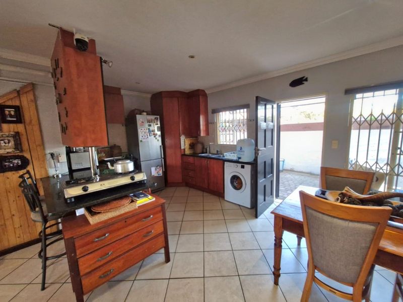 Functional kitchen featuring wooden cabinetry, granite countertops, and tiled flooring, with direct access to an outdoor area through a security-fitted door.