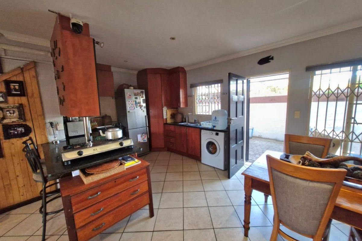 Functional kitchen featuring wooden cabinetry, granite countertops, and tiled flooring, with direct access to an outdoor area through a security-fitted door.