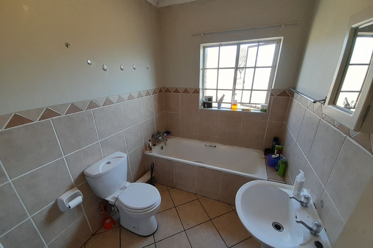 A functional bathroom featuring a bathtub, pedestal basin, and toilet with neutral wall and floor tiling.