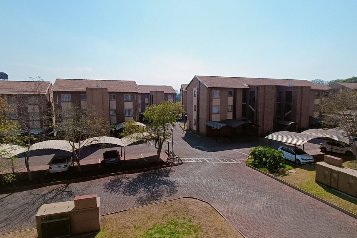 An aerial view of an apartment complex featuring brick buildings, paved driveways, and covered parking bays within a well-maintained residential estate.