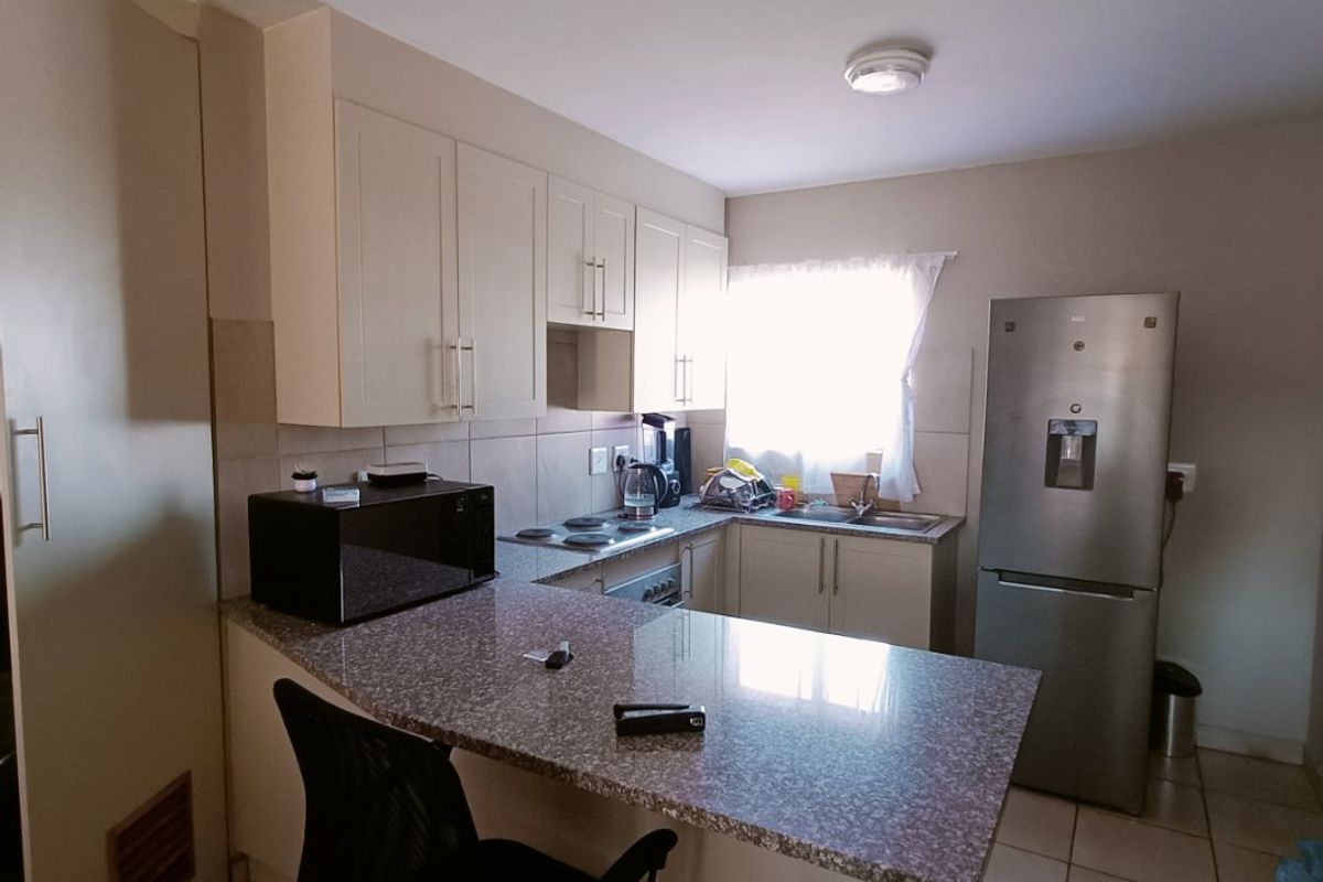 A functional kitchen featuring granite countertops, built-in cabinetry, an electric hob, and a breakfast bar, finished with tiled flooring.