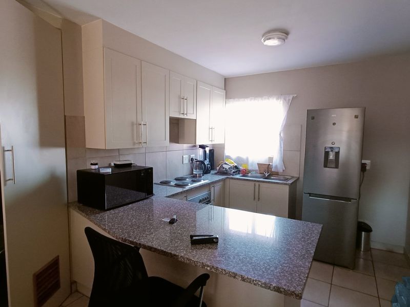 A functional kitchen featuring granite countertops, built-in cabinetry, an electric hob, and a breakfast bar, finished with tiled flooring.