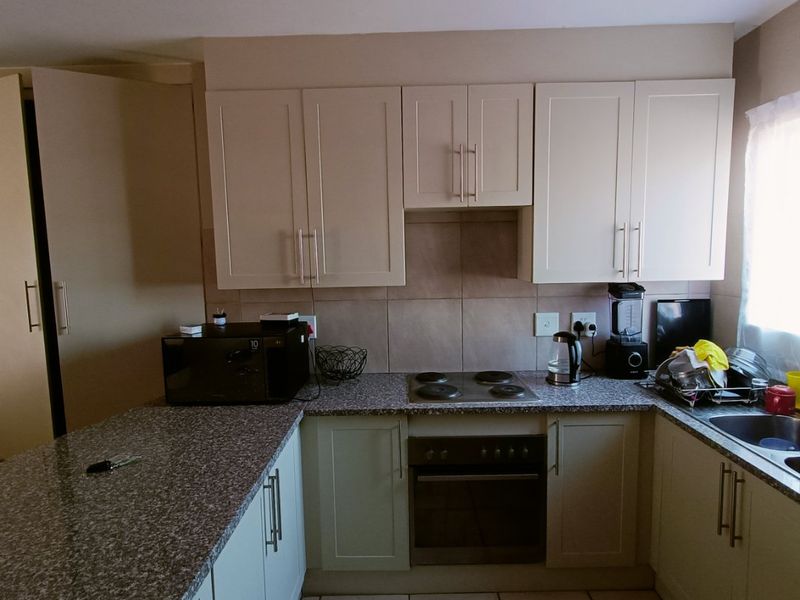 A functional kitchen featuring light-toned cabinetry, granite countertops, a built-in electric oven and hob, and tiled flooring with a neutral backsplash.