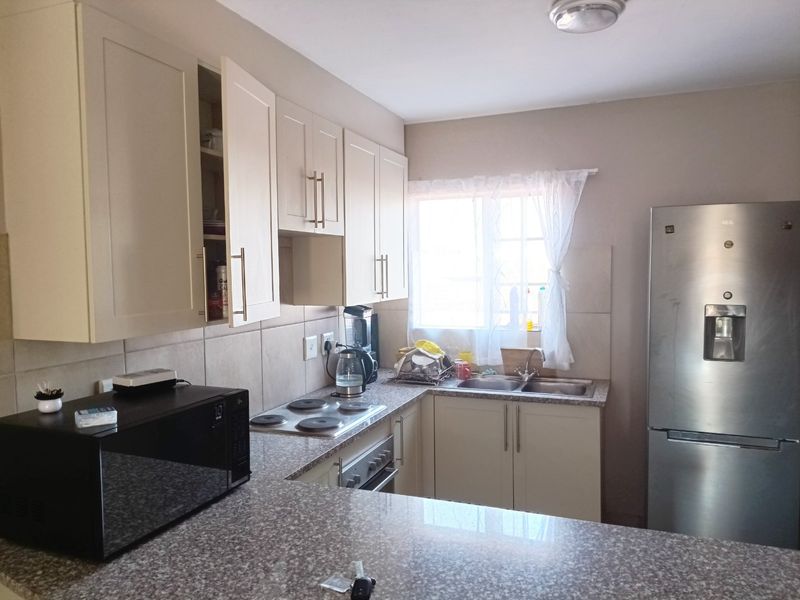 A functional kitchen featuring granite countertops, built-in cabinetry, a stainless steel sink, and an integrated electric hob and oven setup.