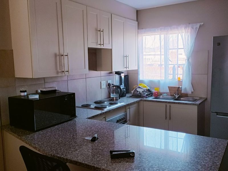 A functional kitchen featuring granite countertops, ample built-in cabinetry, an electric hob, and a stainless steel sink with a window for natural light.