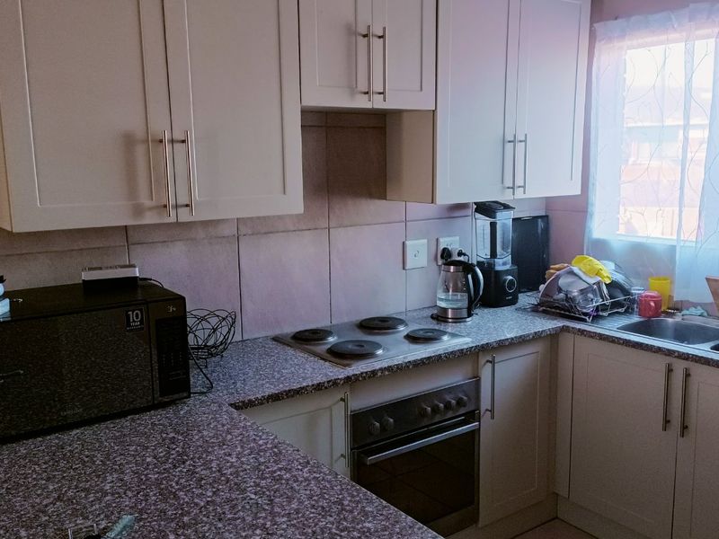 A functional kitchen featuring white cabinetry, granite countertops, a built-in oven with electric hob, and a tiled backsplash.