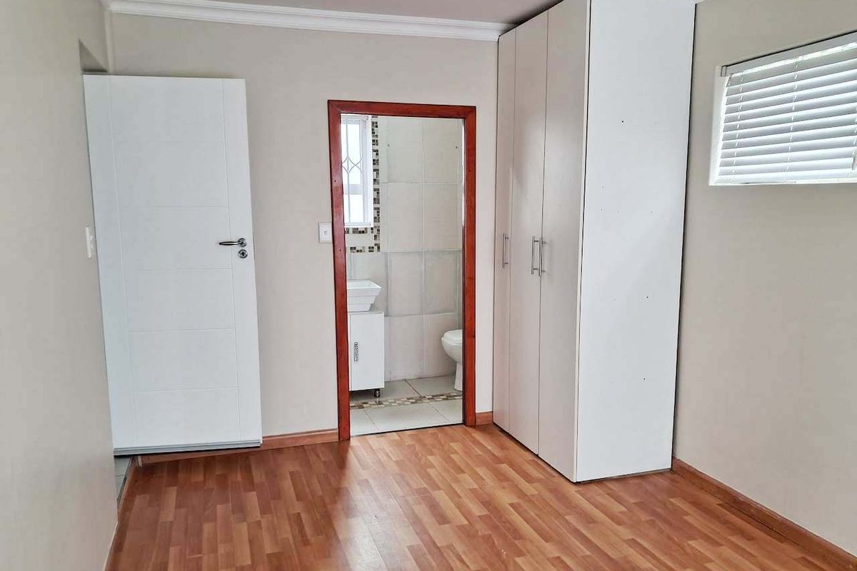 A clean, empty bedroom featuring laminate flooring, a built-in wardrobe, and an adjoining en-suite bathroom with tiled finishes.