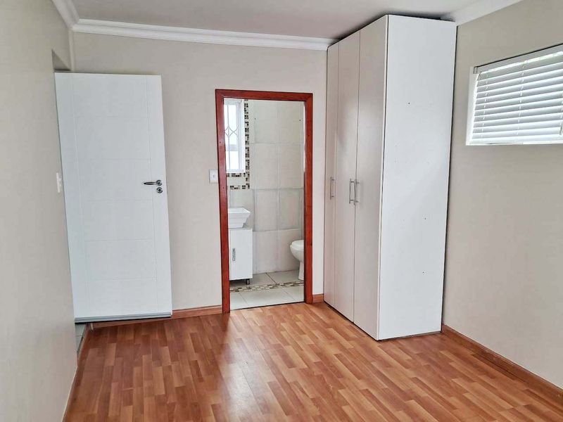 A clean, empty bedroom featuring laminate flooring, a built-in wardrobe, and an adjoining en-suite bathroom with tiled finishes.