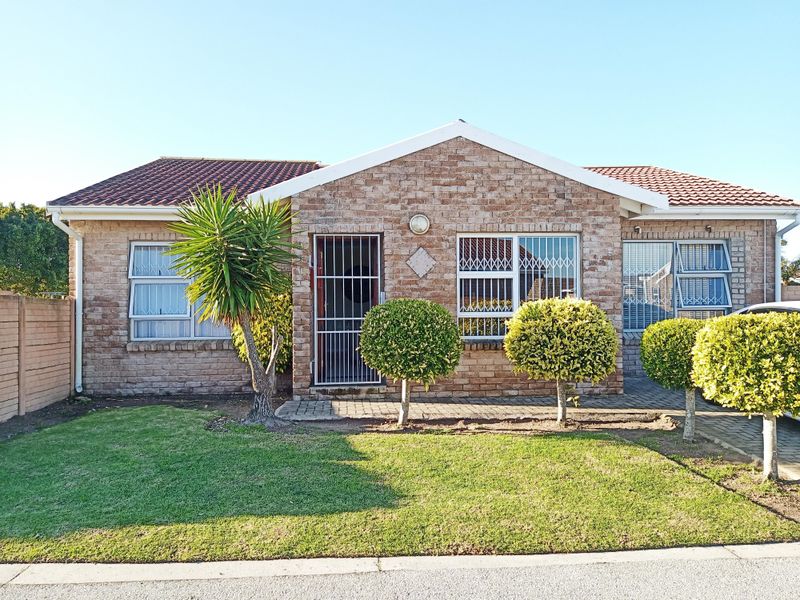 Front elevation of a face brick townhouse featuring a tiled roof, security gates, and a well-maintained front garden with a paved walkway.