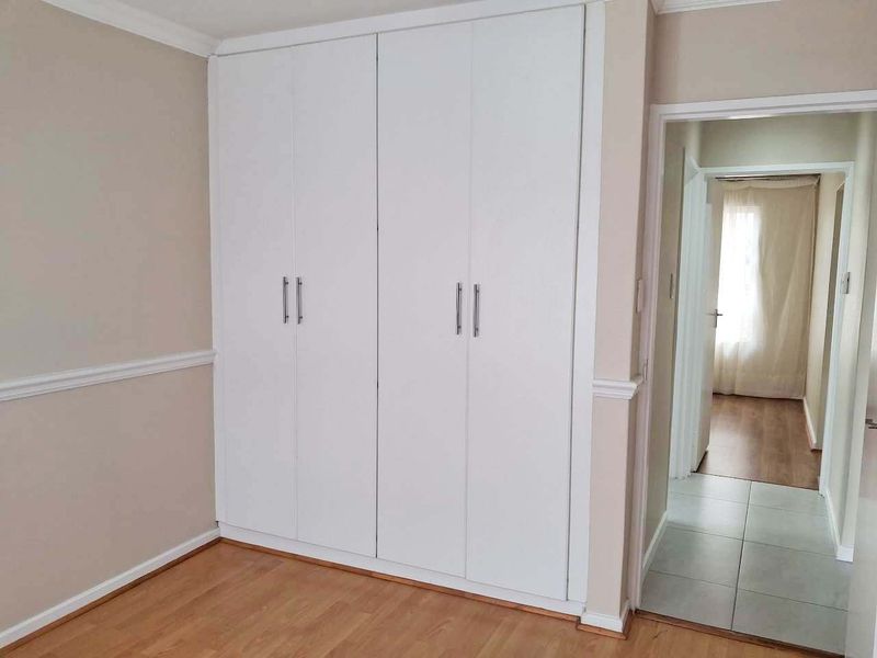 A clean, empty bedroom featuring white built-in wardrobes, laminate flooring, and classic chair rail molding, leading into a tiled hallway.
