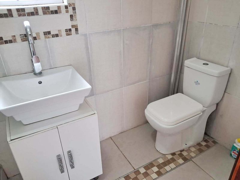 A functional bathroom featuring a modern vessel sink on a white vanity cabinet, tiled walls with decorative accents, and a standard toilet.