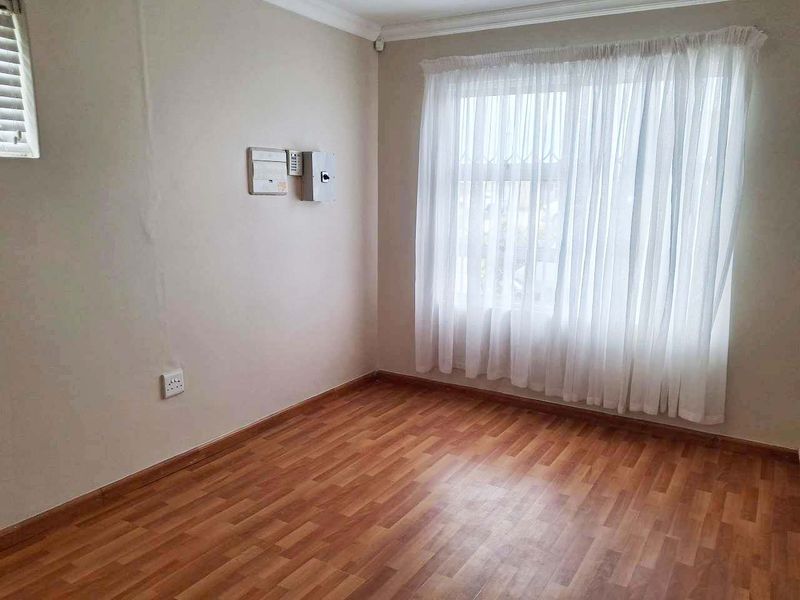 An empty bedroom featuring laminate flooring, neutral walls, and a large window with sheer curtains, ready for personalization.