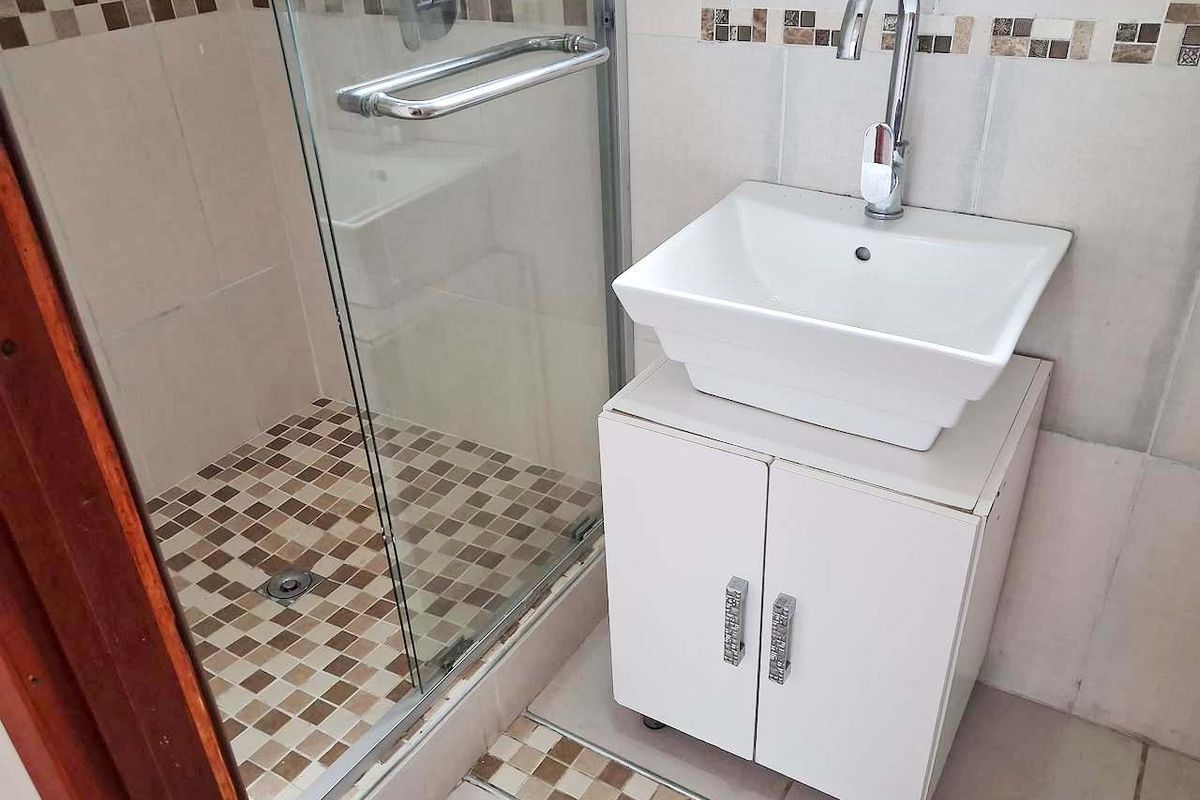 Compact bathroom featuring a vessel sink vanity, chrome fixtures, and a glass-enclosed shower with mosaic tile detailing.
