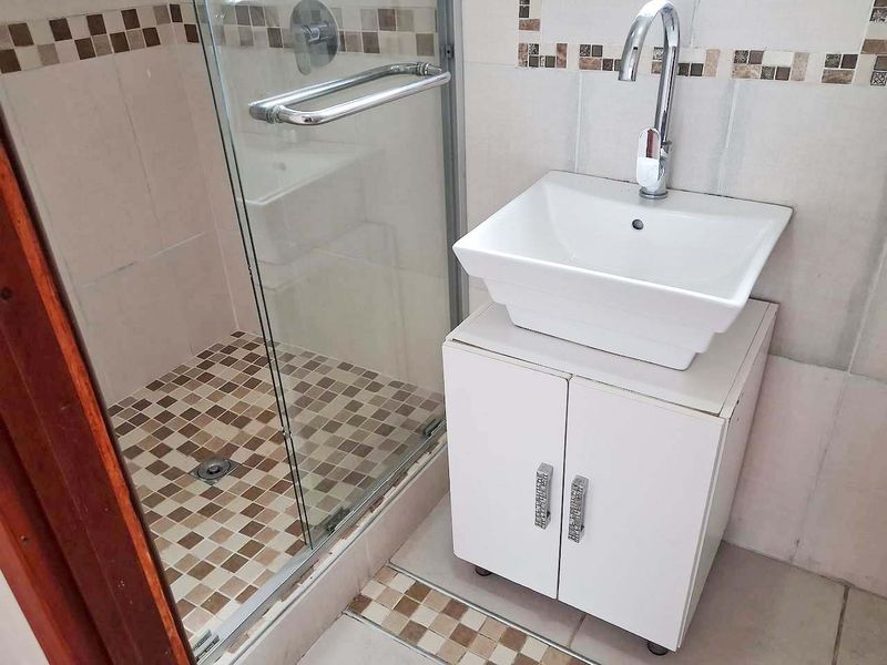 Compact bathroom featuring a vessel sink vanity, chrome fixtures, and a glass-enclosed shower with mosaic tile detailing.