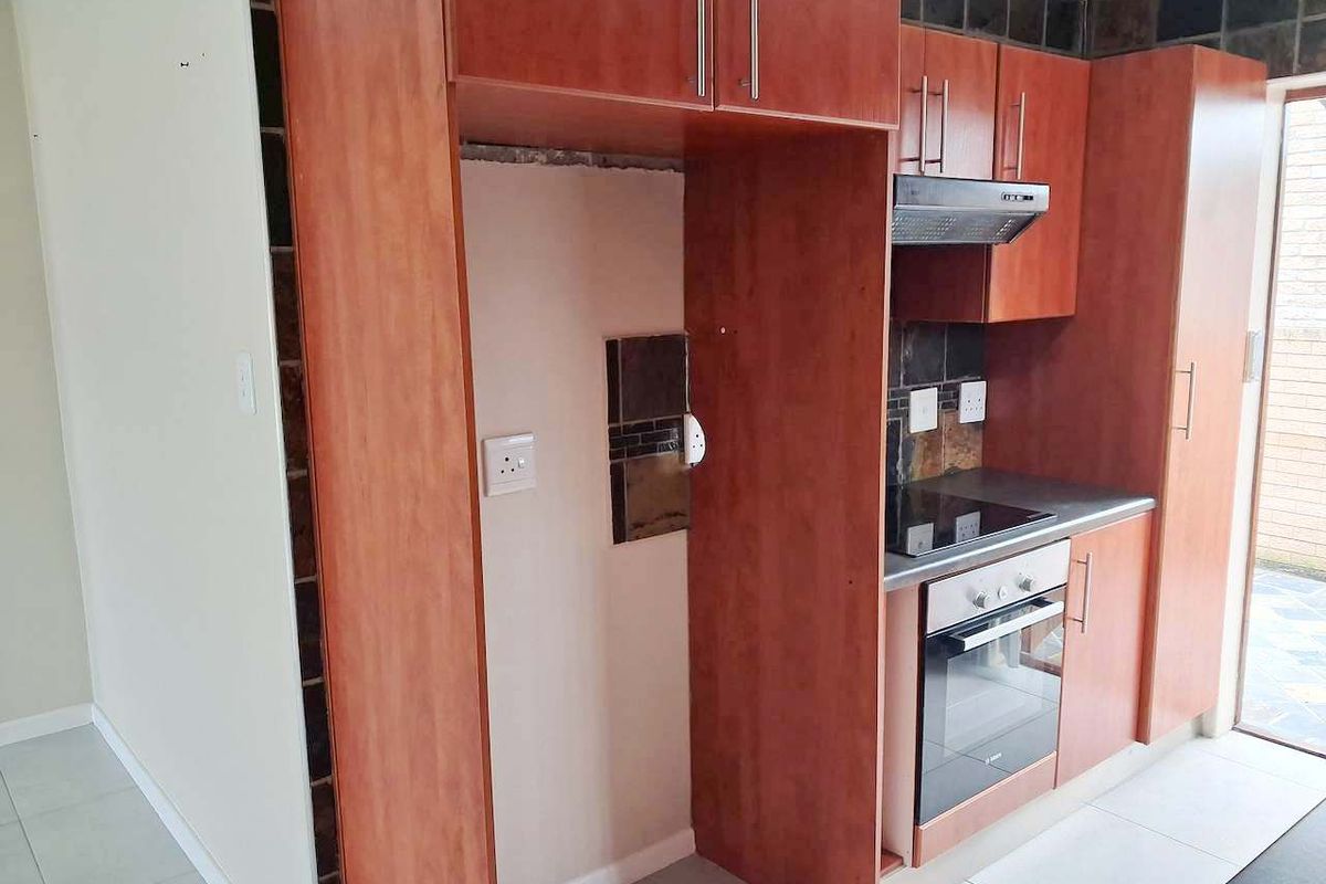 A compact kitchen featuring wood-finish cabinetry, built-in oven and hob, and a tiled backsplash, currently awaiting final finishes and appliance installation.