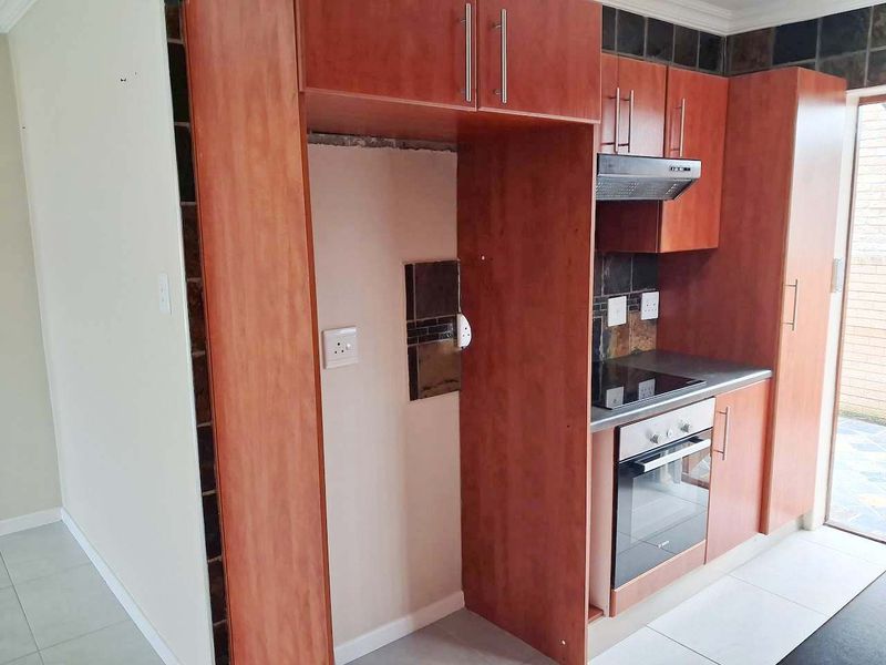 A compact kitchen featuring wood-finish cabinetry, built-in oven and hob, and a tiled backsplash, currently awaiting final finishes and appliance installation.