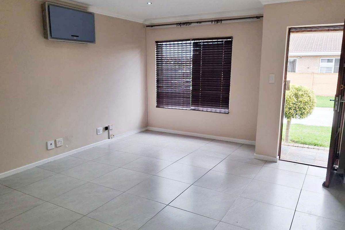 A bright, empty living room featuring neutral tiled flooring, recessed downlighting, and a wall-mounted air conditioning unit, with direct access to the exterior.