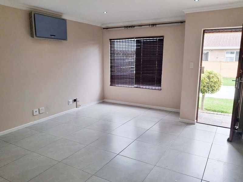 A bright, empty living room featuring neutral tiled flooring, recessed downlighting, and a wall-mounted air conditioning unit, with direct access to the exterior.