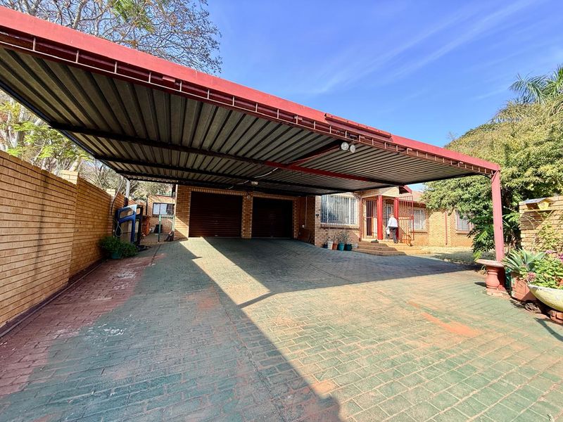Front exterior view featuring a large double carport, double garage doors, and a paved driveway with brick boundary walls.