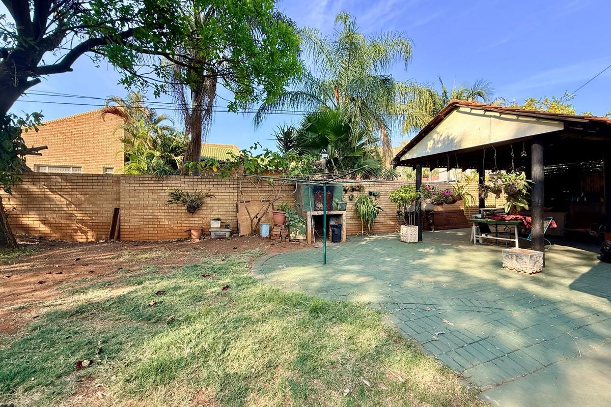 Spacious rear garden featuring a paved patio area, a covered entertainment space, and a built-in braai, offering potential for outdoor living and landscaping.