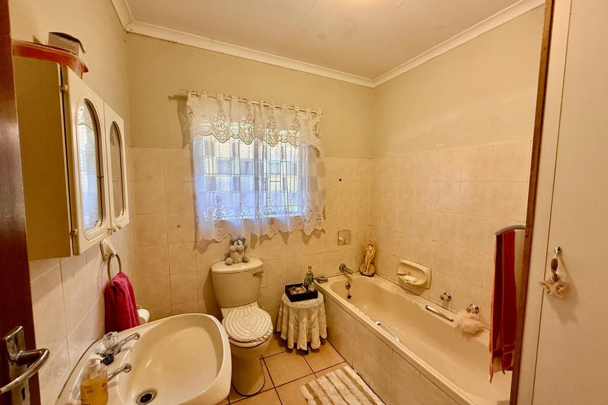 A dated bathroom featuring a standard bathtub, pedestal basin, and toilet with neutral wall tiling and floor tiles.