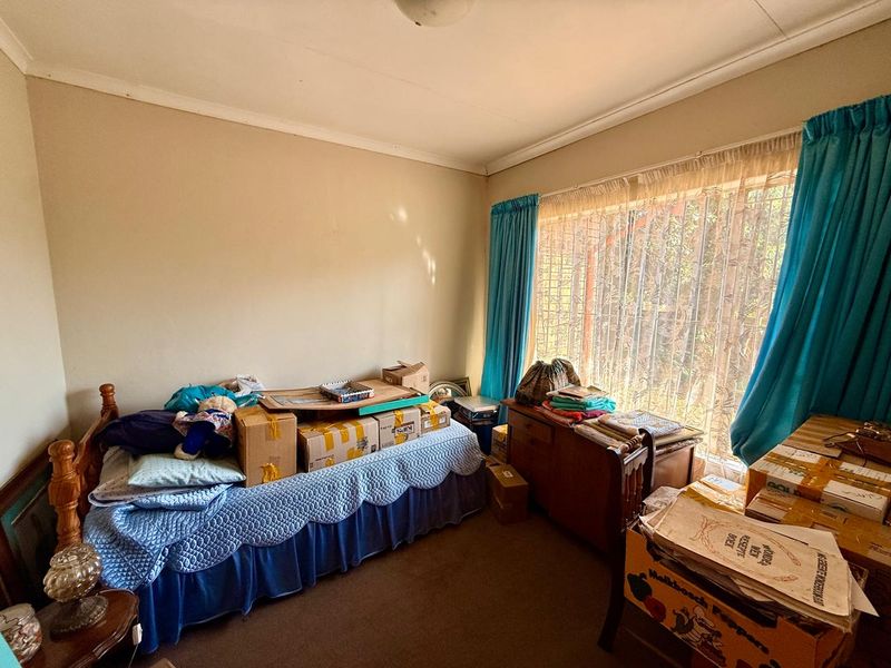 A bedroom featuring carpet flooring, curtain rails, and a security gate over the window, currently used for storage.