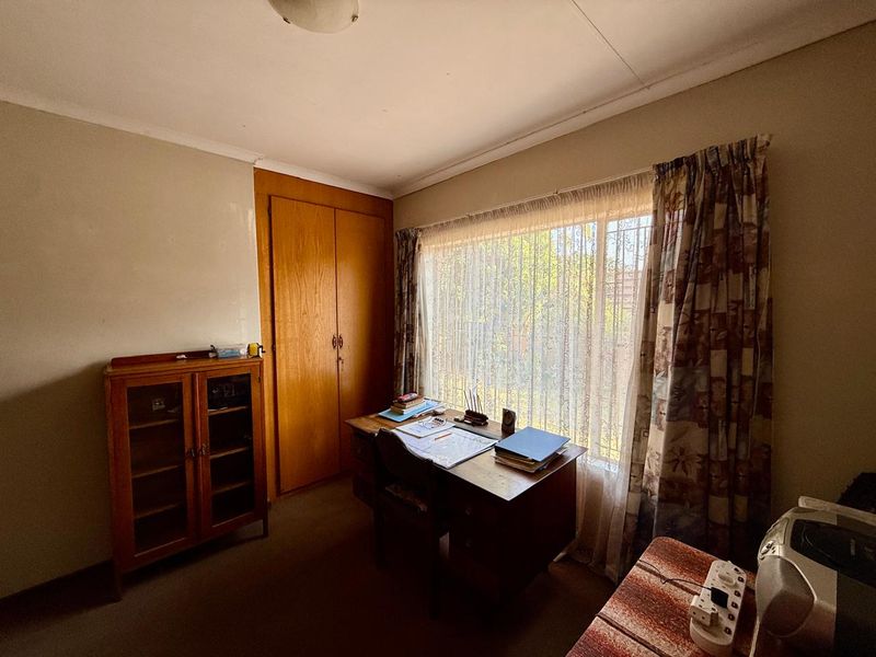 A bedroom featuring a built-in wooden cupboard and a large window, providing natural light. The room requires cosmetic updates to modernize the finishes.